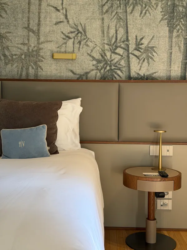 Layered linens, a velvet cushion and a brass bedside lamp