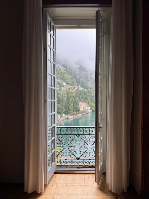 Open balcony doors framing Lake Como and the surrounding hillside