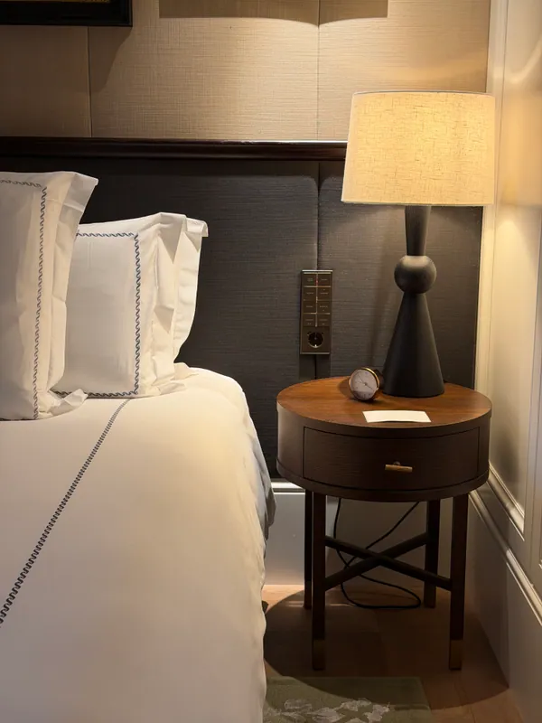Embroidered white bed linens and a softly lit bedside table